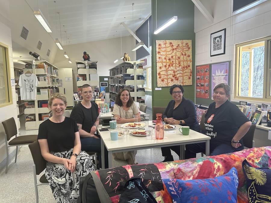 Five women sitting around a table smiling.