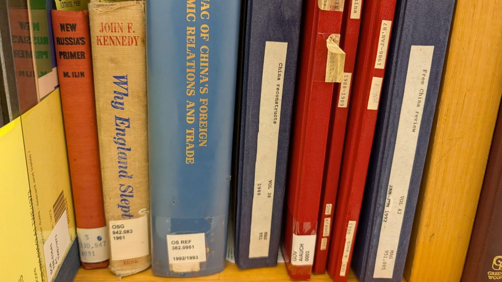 Rows of books on library shelves with labels and spine titles visible