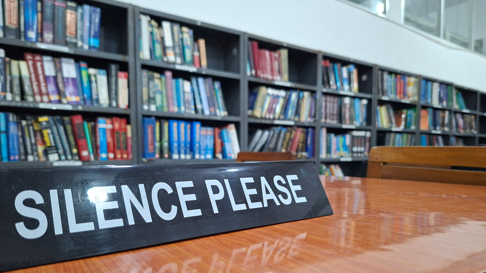 ‘Silence’ sign on library desk with bookshelves in the background